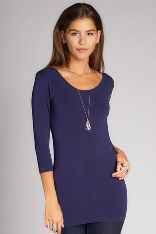A woman wearing a purple 3/4 sleeve scoop neck top made of bamboo, cotton, nylon, and spandex.